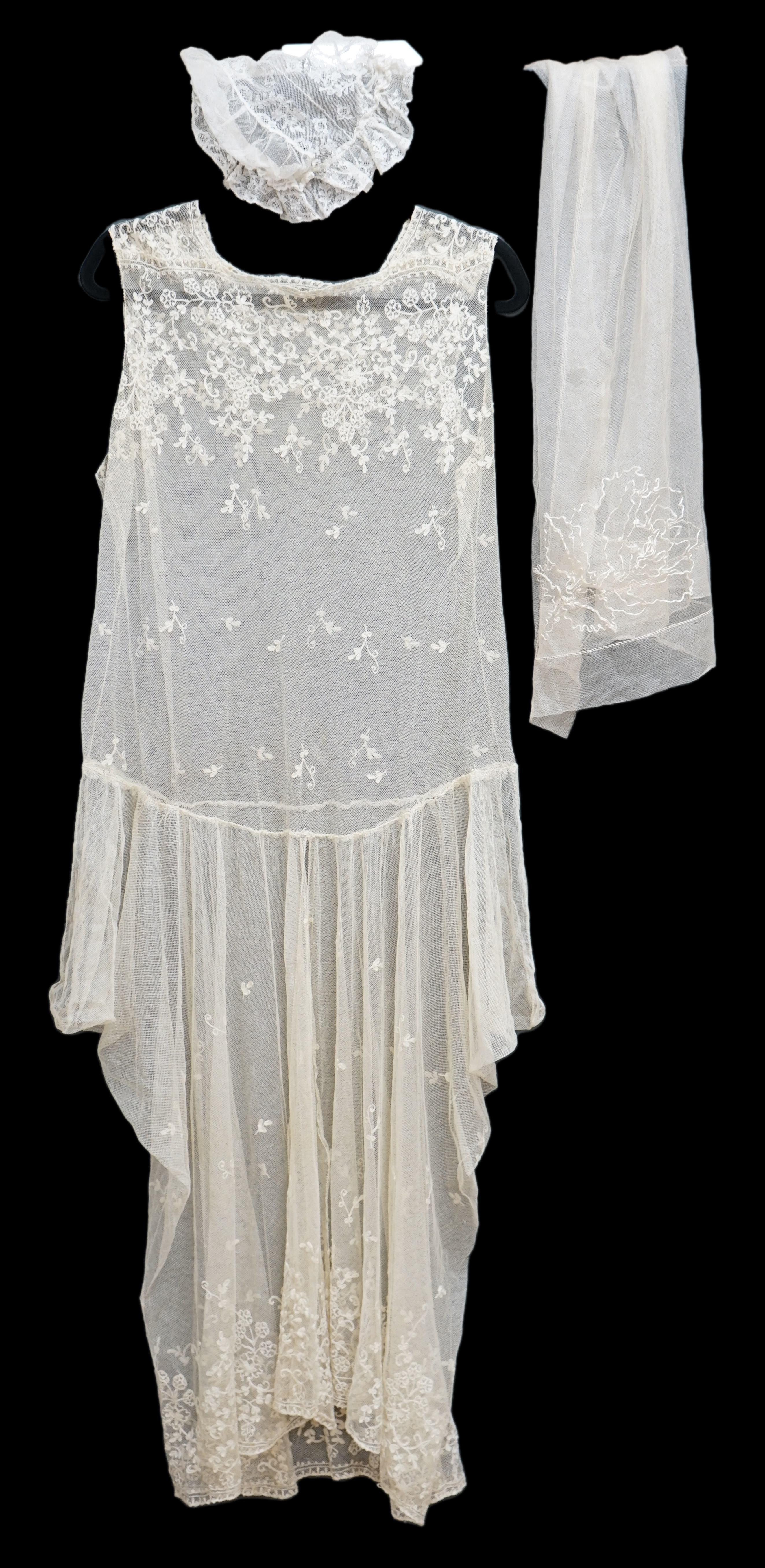 A 1920's cream net and needle run, lace wedding dress, together with a small silk net veil, and lace boudoir cap, the dress worked with a deep needle run bodice and skirt edge, with all over sprig motifs, designed with a